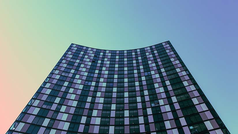 A down-up view of a tall curved glass building with a blue background