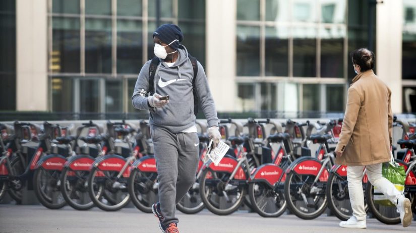 A man with a facemask on walks with bicycles lined up behind him