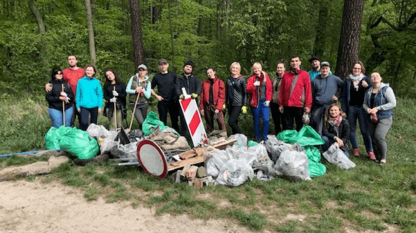 Several people gathered together with a pile of plastics and trash lied in front of them after a long clean up with the forest in the background